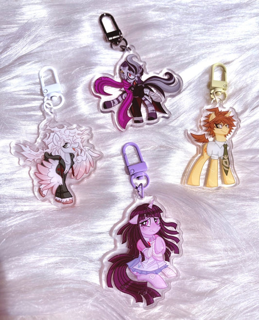 Four anime character acrylic keychains arranged on a white faux fur background. The keychains feature different characters with distinct colors including purple, pink, orange, and white, each attached to a metal clasp.