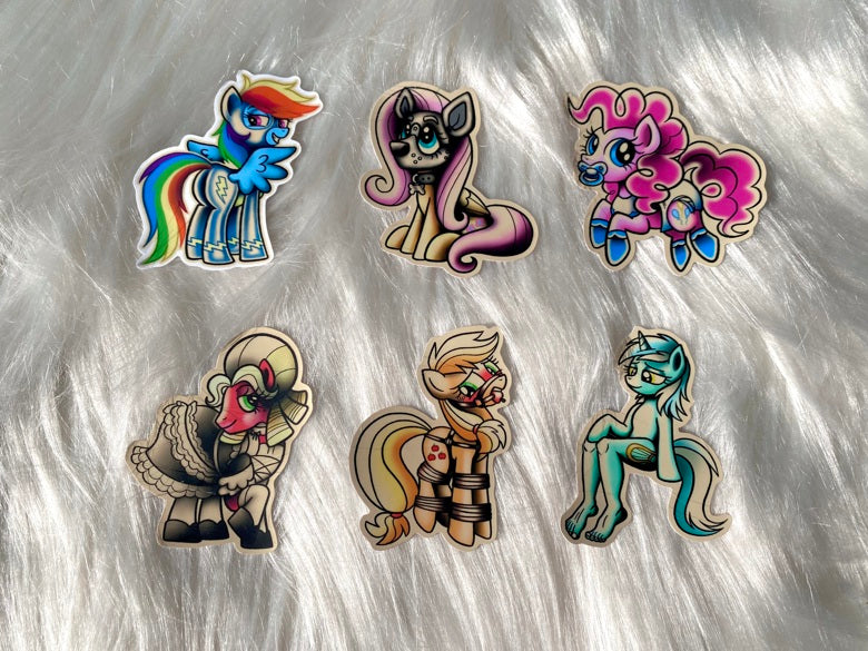 Six die-cut vinyl stickers featuring various colorful cartoon pony characters, arranged on a white faux fur background.