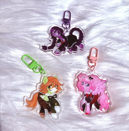 Three acrylic keychains featuring anime-style pony characters, displayed on a white faux fur background. The keychains include a purple-haired character with a silver clasp, an orange-haired character with a green clasp, and a pink-haired character with a pink clasp.